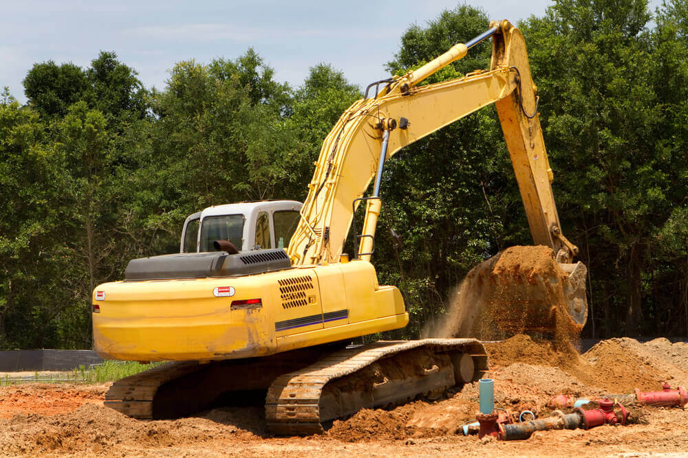 an excavator cutting out a section of dirt and filling in a low area of the work site