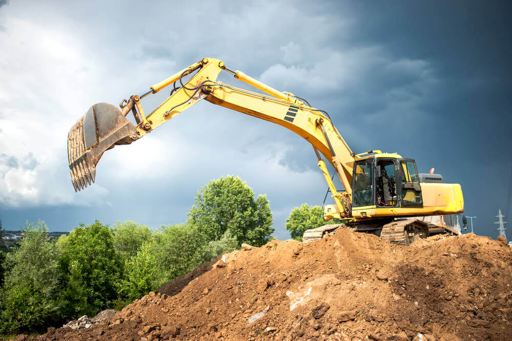a yellow excavator reaching out its arm to get some dirt from the lower area of the mound that it sits on