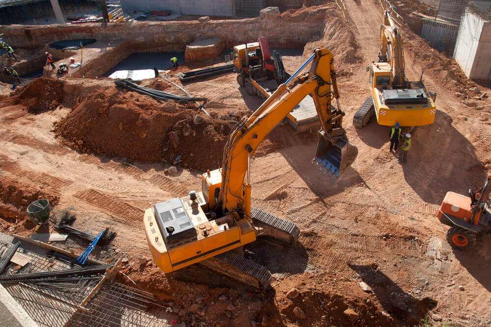 2 large excavators in a work site that has been cut out with several earth moving machines close by
