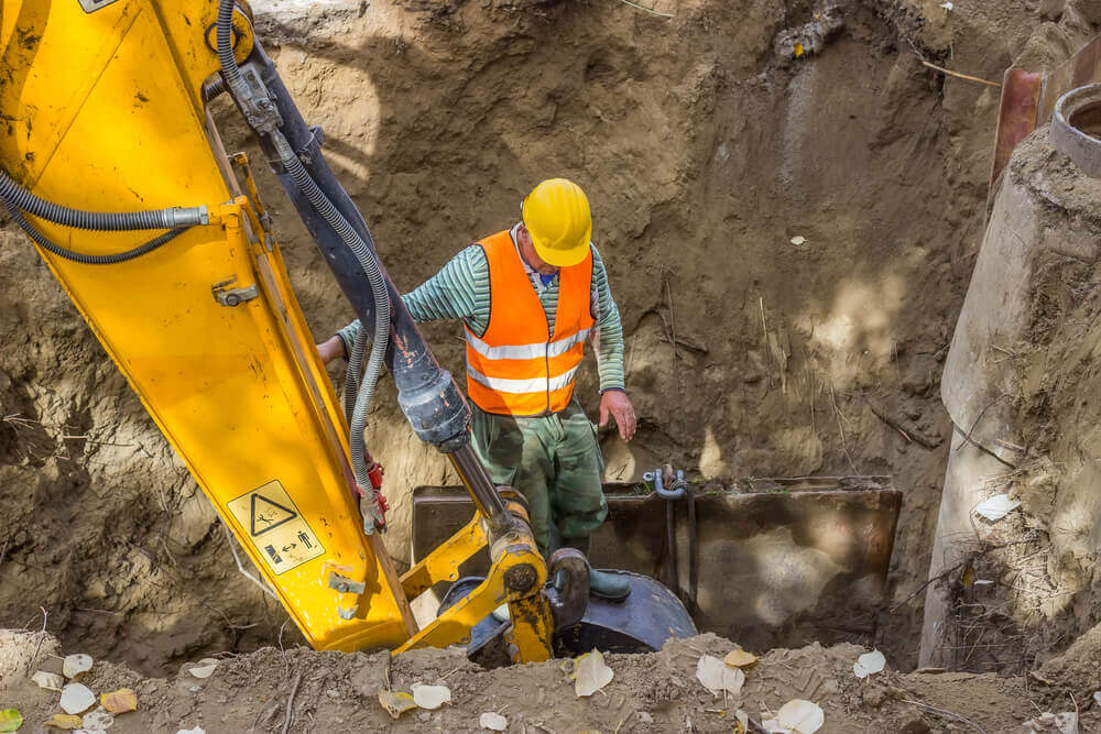 an excavator digging a deep hole with a worker with high-vis on inspecting the bottom of the hole